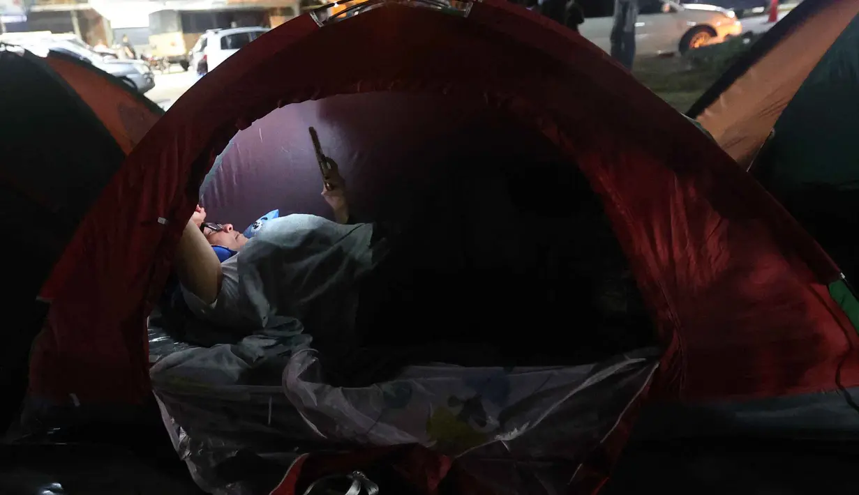 Mereka dengan cemas menanti pembebasan tahanan politik yang telah dijanjikan. Tampak dalam foto, seorang wanita menggunakan telepon seluler di atas tenda yang didirikan oleh kerabat tahanan politik di luar penjara El Rodeo I di Guatire, Negara Bagian Miranda, sekitar 30 kilometer sebelah timur Caracas, Venezuela, pada 12 Januari 2026. (Pedro MATTEY/AFP)