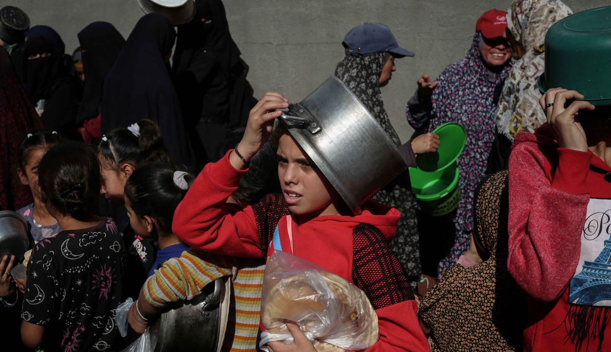 Rencana peningkatan bantuan kemanusiaan yang terperinci telah dibuat, termasuk penyediaan makanan, air bersih, tempat tinggal, dan pasokan medis, tetapi pelaksanaannya terhambat oleh pembatasan yang ada. Tampak dalam foto, warga Palestina yang terlantar, anak-anak, dan dewasa, menunggu makanan di sebuah tempat penampungan yang telah dihuni keluarga-keluarga di Nuseirat, pusat Jalur Gaza, pada 23 November 2025. (EYAD BABA/AFP)