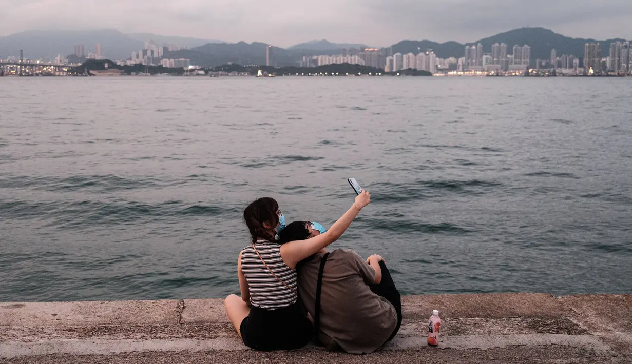 Pasangan berselfie di dermaga kargo yang dijuluki 'Dermaga Instagram' di Hong Kong (21/4/2020). Hong Kong melaporkan penurunan kasus infeksi harian Covid-19, tetapi pemerintah kota mengatakan mereka tidak mengambil risiko apa pun. (AFP/Anthony Wallace)