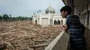 Di antara tumpukan pohon tersebut, terdapat bangunan masjid dengan kubah berwarna hijau yang masih kokoh berdiri. Tampak dalam foto, warga menyaksikan tumpukan pohon tumbang yang tersapu banjir bandang sekitar tiga minggu lalu dari koridor lantai dua yang tergenang air di Pesantren Darul Mukhlisin dan masjid yang terhubung dengan pesantren tersebut di Aceh Tamiang, pada Minggu 14 Desember 2025. (Yasuyoshi CHIBA/AFP)