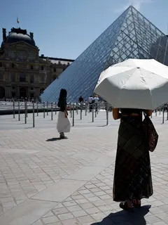 Seseorang berlindung di bawah payung di depan museum Louvre di Paris saat gelombang panas yang memecahkan rekor melanda sebagian besar Eropa Barat pada Kamis 28 Mei 2026. (SIMON WOHLFAHRT/AFP)