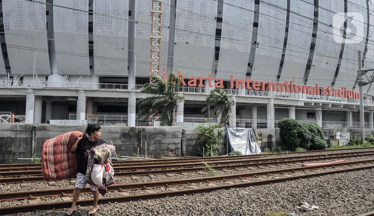 Warga melewati rel kereta yang bersebelahan dengan Jakarta International Stadium, Kelurahan Papanggo, Tanjung Priok, Jakarta Utara, Selasa (22/2/2022). Sekitar 130 rumah semipermanen di kawasan Pela-Pela jadi pemandangan kontras dengan megahnya JIS. (merdeka.com/Iqbal S Nugroho)
