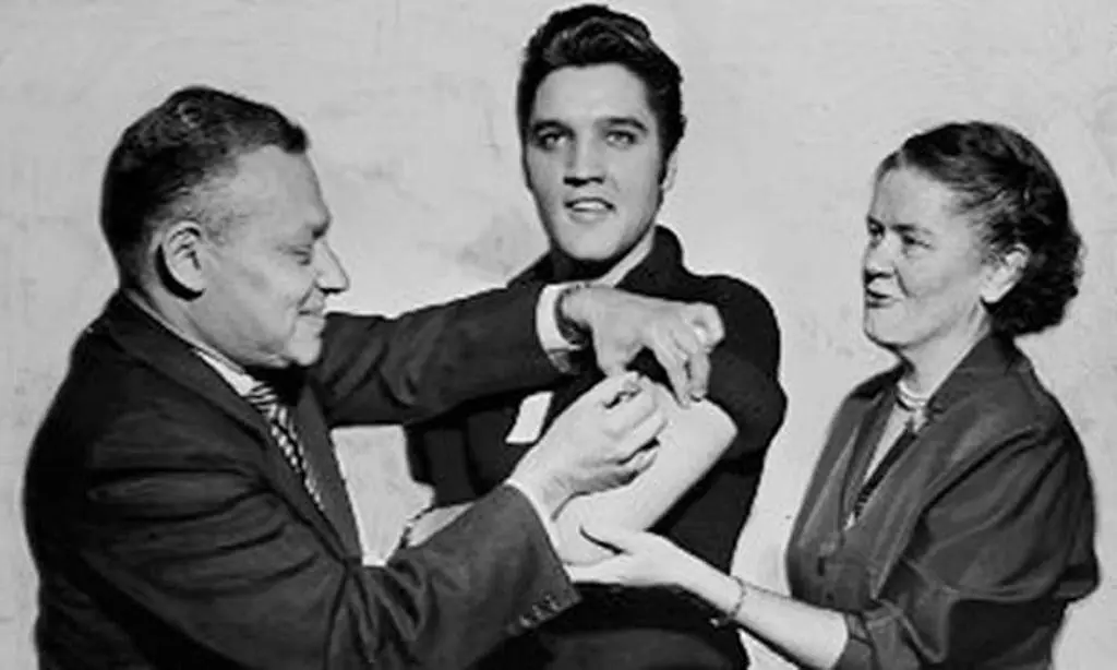 Elvis Presley menerima vaksin polio dari dokter di CBS studios, New York,  1956. ( Seymour Wally/NY Daily News via The Guardian)