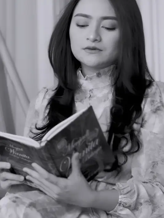 Lalu adegan berlanjut, ia duduk sebuah kursi goyang sambil memegang sebuah buku berjudul Menjadi Wanita Paling Bahagia. (@nathalieholscher)