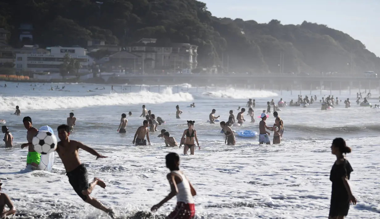 Orang-orang menikmati pantai di dekat Pulau Enoshima (punggung L) di pantai Prefektur Kanagawa, barat daya Tokyo, (13/8/2019). Secara administratif, Enoshima adalah bagian dari kota daratan Fujisawa, dan terhubung ke bagian Katase di kota itu dengan jembatan sepanjang 2.000 meter. (AFP Photo/Charly