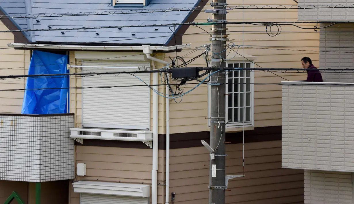 Seorang pria berada di samping rumah yang ditutupi kain biru di mana polisi menemukan sembilan mayat termasuk dua kepala yang disimpan di kotak pendingin di Zama, Prefektur Kanagawa, Jepang, (31/10). (AFP Photo/Toru Yamanaka)