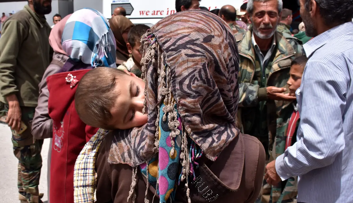 Seorang anak tertidur dalam gendongan saat berada di sebuah tempat penampungan sementara di Jibrin di pinggiran timur Aleppo, Jumat (21/4). Pengungsi adalah warga dari kota Fuaa dan Kafraya. (AFP PHOTO / George OURFALIAN)