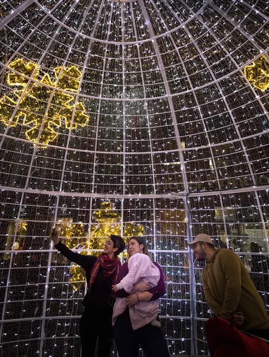 Keluarga berselfie di bawah lampu Natal yang menghiasi jalan Santa Cruz de Tenerife di pulau Canary Tenerife, Spanyol (19/12). Menyambut Natal kota Tenerife memasang lampu warna-warni untuk menghiasi sejumlah jalanan. (AFP Photo/Desiree Martin)