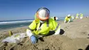 Seorang pekerja dengan pakaian pelindung membersihkan pantai yang terkontaminasi tumpahan minyak di Huntington Beach, California, Amerika Serikat, Selasa (5/10/2021). Kebocoran pipa menyebabkan tumpahan minyak di lepas pantai California. (AP Photo/Ringo H.W. Chiu)