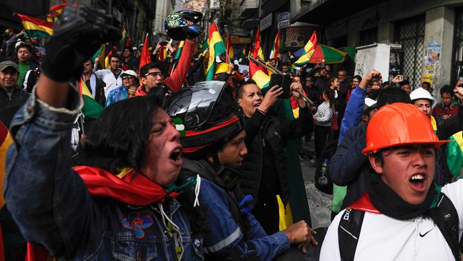 Orang-orang mengibarkan bendera Bolivia merayakan pengunduran diri Presiden Evo Morales di La Paz, Minggu (10/11/2019). Morales memutuskan mengundurkan diri buntut aksi protes yang dilatarbelakangi dugaan dirinya melakukan kecurangan dalam pemilu dalam beberapa pekan terakhir. (JORGE BERNAL/AFP)