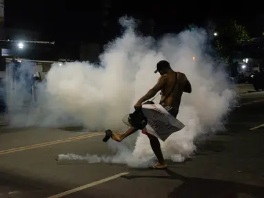 Seorang penduduk favela Cidade de Deus (Kota Tuhan) menendang tabung gas air mata yang ditembakkan oleh polisi selama protes di kota kumuh di Rio de Janeiro, Brasil, pada 7 Agustus 2023. (AFP/Tercio Teixeira)