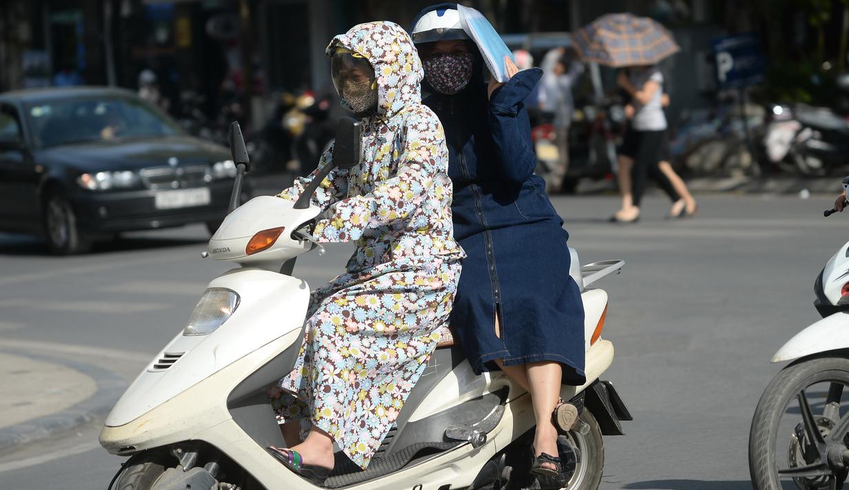 Seorang wanita pengendara motor dan rekannya menggunakan pakaian pelindung saat melintasi pusat kota Hanoi, Rabu (15/6). Vietnam menghadapi gelombang panas dengan suhu hingga mencapai 40 derajat celcius. (Hoang DINH NAM/AFP)