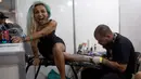Ekspresi seorang wanita saat kakinya ditato dalam acara Tattoo Week tahunan di Rio de Janeiro, Brasil (12/1). Ajang perhelatan seniman dan penggemar tato ini diadakan setiap tahunnya di Brasil. (AFP Photo/Mauro Pimentel)