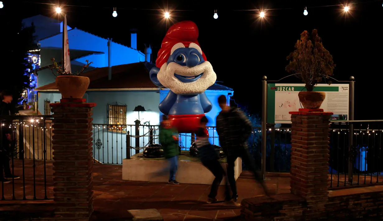 Anak-anak bermain bola di dekat patung karakter Smurf di desa serba biru di Juzcar, Selatan Spanyol, 2 Desember 2016. Kini desa serba biru tersebut menjadi sangat populer sebagai desa Smurfs bagi wisatawan. (REUTERS/Jon Nazca)