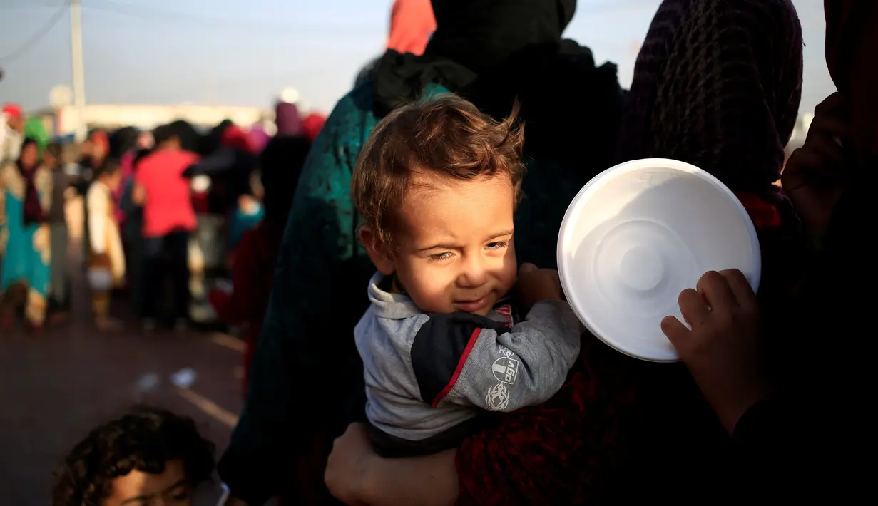<p>Seorang wanita pengungsi membawa anaknya saat mengantri untuk menerima makanan dari Barzani Charity Foundation (BCF) di sebuah kamp untuk pengungsi di pinggiran Erbil, Irak, Senin (31/10). (REUTERS / Zohra Bensemra)</p>