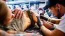 Seorang seniman mentato badan pengunjung wanita dalam acara edisi keempat Montreux Tattoo Convention di Montreux, Swiss  (22/9). Lebih 150 seniman tato dari 22 negara berkumpul dalam acara tersebut. (Valentin Flauraud/Keystone via AP)