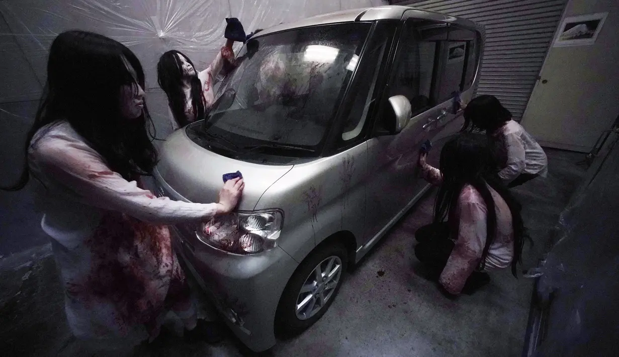 Para pemeran zombie membersihkan darah palsu pada kendaraan saat demonstrasi pertunjukan rumah hantu drive-in di Tokyo, Jepang, Selasa (18/8/2020). Rumah hantu drive-in ini diadakan di tengah pandemi COVID-19. (AP Photo/Eugene Hoshiko)