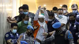 M Rizieq Shihab (tengah) mengangkat tangan saat meninggalkan gedung Ditreskrimum Polda Metro Jaya, Jakarta, Minggu dini hari (13/12/2020). Rizieq Shihab ditahan setelah menjalani pemeriksaan sebagai tersangka penghasutan dan kerumunan di tengah pandemi COVID-19. (Liputan6.com/Helmi Fithriansyah)