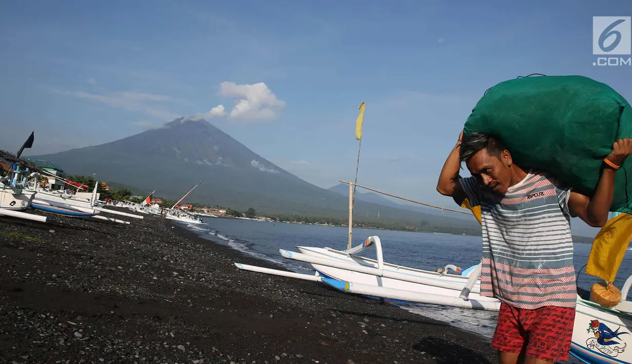 Nelayan membawa hasil tangkapannya dengan latar Gunung Agung di kawasan Amed, Karangasem, Bali, Kamis (7/12). Sepekan terakhir, aktivitas Gunung Agung mulai tampak tenang, meskipun masih status Awas. (Liputan6.com/Immanuel Antonius)