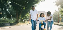 Anak perempuan sedang bermain sepeda bersama ibu dan ayahnya. Credits: pexels.com/panditwiguna.