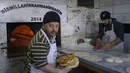Para pekerja mengumpulkan roti di toko roti yang membagikan roti gratis di Samandag, selatan Hatay pada 16 Februari 2023, sepuluh hari setelah gempa berkekuatan 7,8 melanda wilayah perbatasan Turki dan Suriah.  Lusinan tangan dengan panik meraih pemanas dan selimut yang dibagikan oleh donor swasta, menggambarkan keputusasaan dan kemarahan yang mencengkeram wilayah Turki 11 hari setelah bencana gempa. (Photo by Yasin AKGUL / AFP)