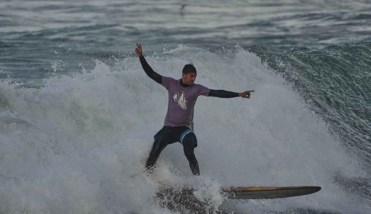 Namun, area ini tetap menjadi tempat pelarian bagi warga untuk mencari ketenangan dari tekanan situasi politik dan sosial. Tampak dalam foto, Tahseen Abu Assi, warga Palestina, berselancar di pantai Kota Gaza, Minggu, 28 Desember 2025. (AP Photo/Jehad Alshrafi)