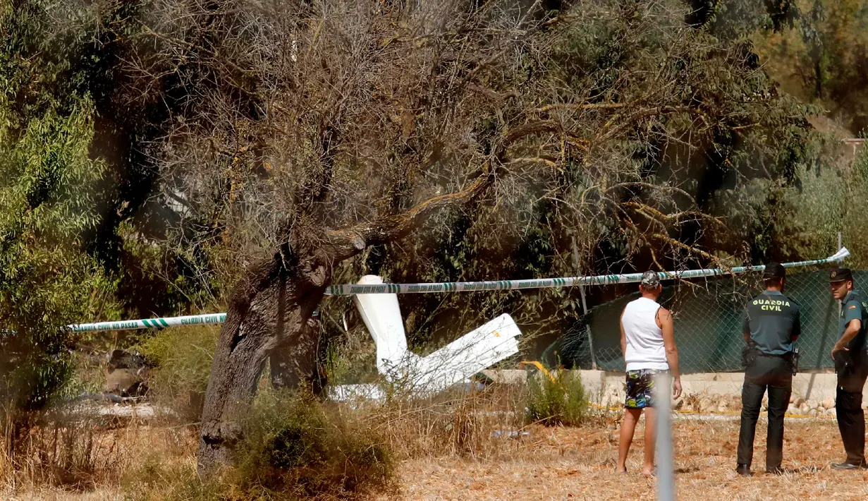Polisi sipil Guardia Spanyol berdiri dekat puing-puing setelah helikopter dan pesawat kecil tabrakan di dekat Inca, Pulau Mallorca, Minggu (26/8/2019). Namun sampai saat ini, kepolisian dan otoritas setempat belum menyimpulkan penyebab tabrakan udara tersebut. (STRINGER / AFP)