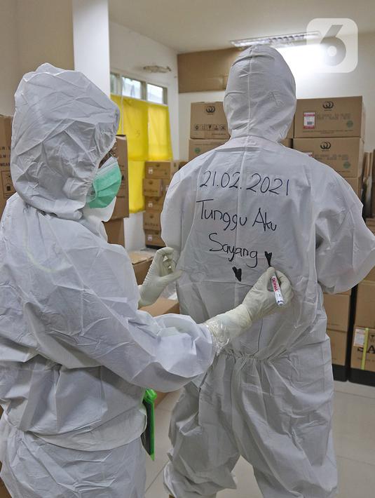 Tenaga kesehatan menulis bagian belakang pakaian APD rekannya di RSDC Wisma Atlet, Jakarta, Selasa (26/1/2021). Data Satgas Covid-19 per Selasa (26/1) mencatat kasus COVID-19 di Indonesia bertambah 13.094 sehingga total menyentuh satu juta, tepatnya 1.012.350. (Liputan6.com/Herman Zakharia)