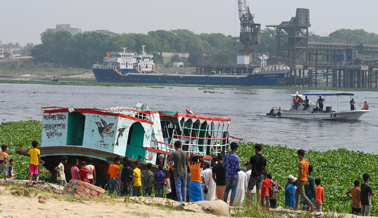 Orang-orang menyaksikan petugas pemadam kebakaran mencari korban kecelakaan feri di Sungai Shitalakshya di Narayanganj, Bangladesh (21/3/2022). Setidaknya enam mayat ditemukan dan 20 orang masih hilang setelah sebuah feri terbalik di sungai Shitalakkhya. (AFP/Munir uz Zaman)