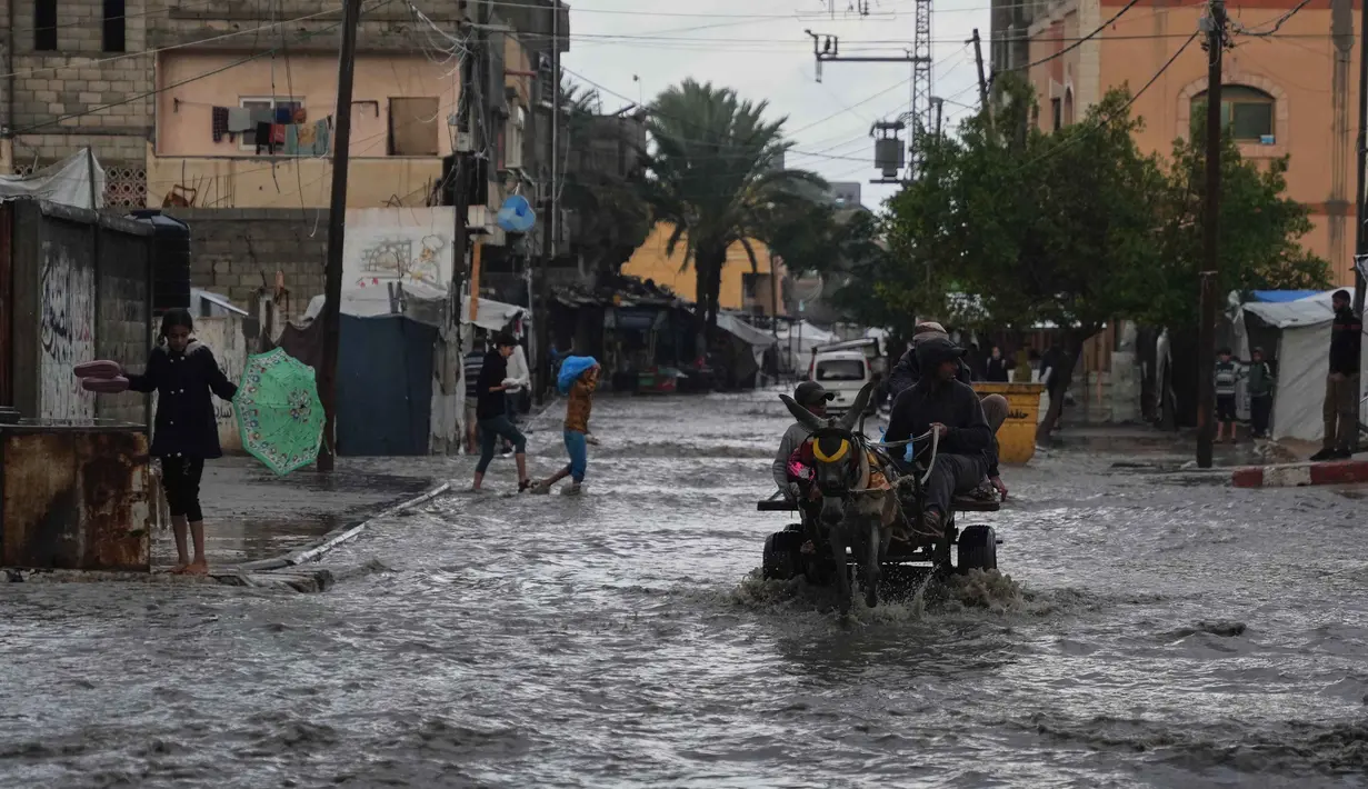Serangan Israel juga memaksa sebagian besar warga untuk mengungsi ke tenda-tenda yang tidak memberikan perlindungan maksimal. Tampak dalam foto, warga Palestina berjalan di jalanan yang terendam banjir setelah hujan deras di Deir al-Balah, Jalur Gaza tengah, Selasa 25 November 2025. (AP Photo/Abdel Kareem Hana)