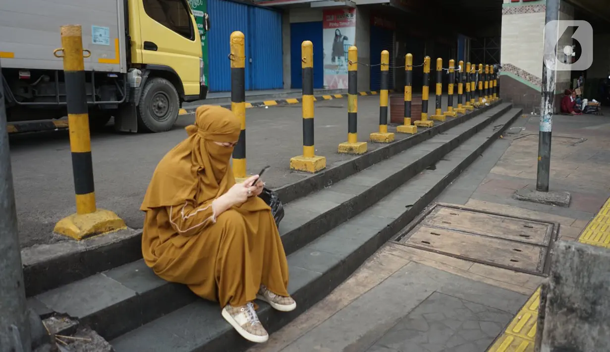 Seorang wanita mengoperasikan gawainya saat duduk di kawasan Pasar Tanah Abang, Jakarta, Senin (11/5/2020). Pemerintah Provinsi DKI Jakarta kembali memperpanjang penutupan sementara Pasar Tanah Abang hingga 22 Mei 2020 untuk mencegah penyebaran virus corona COVID-19. (Liputan6.com/Immanuel Antonius)