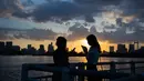 Dua wanita bermain ponsel mereka saat matahari terbenam di Odaiba, Tokyo, (29/7). Nama "Odaiba" berasal dari sebutan untuk enam pulau di Teluk Tokyo yang dibangun sebagai benteng oleh Keshogunan Tokugawa. (AFP Photo/Martin Bureau)