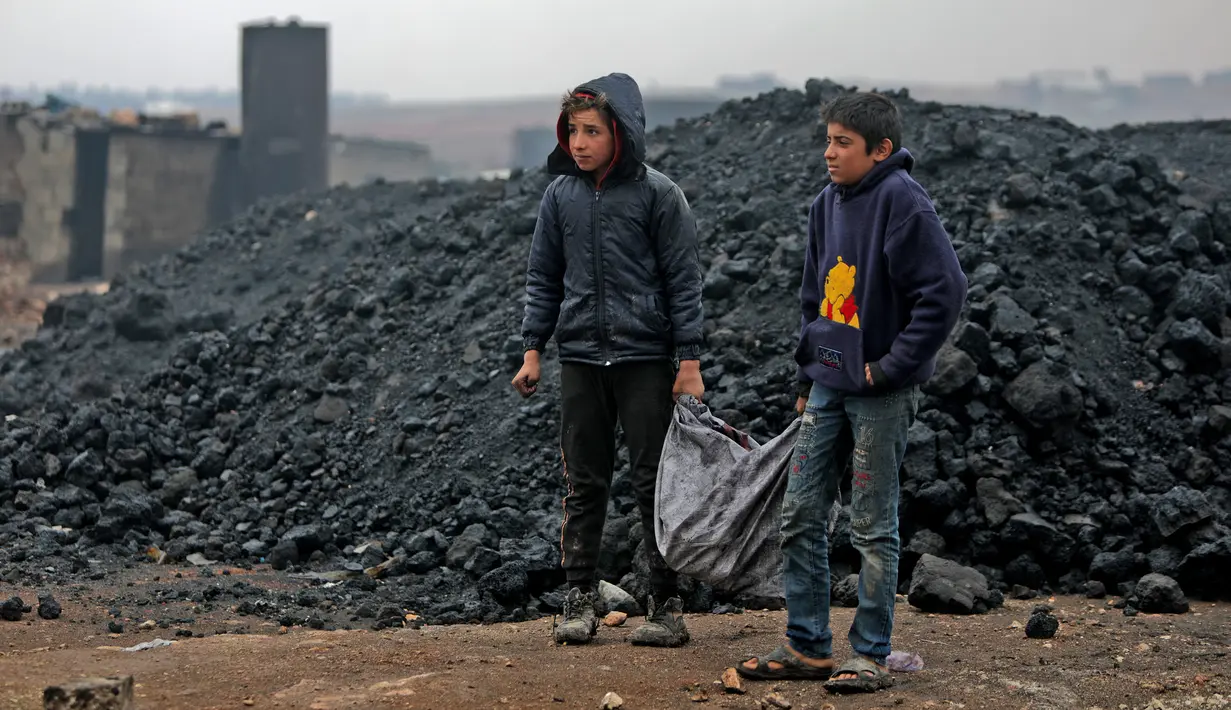 Dua anak Suriah mengangkut batu bara saat mereka bekerja di kilang minyak darurat dekat Kota al-Bab yang dikuasai Turki, Suriah, 20 November 2021. Sebanyak 1,6 juta anak Suriah juga berisiko putus sekolah. (Bakr ALKASEM/AFP)