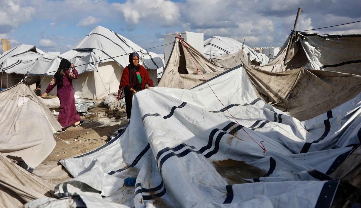 Para pengungsi di Gaza hanya punya dua pilihan tempat berlindung. Tampak dalam foto, seorang perempuan Palestina pengungsi merapikan terpal tenda keluarga saat wilayah tersebut dilanda hujan dan kondisi musim dingin yang dingin, di Kota Gaza pada 28 Desember 2025. (Omar AL-QATTAA/AFP)