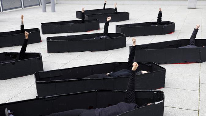 Para wanita mengangkat tangan yang terkepal saat berbaring dalam peti mati tiruan untuk mewakili mereka yang tewas jelang Hari Perempuan Internasional di luar Pengadilan Distrik, Tel Aviv, Israel, Minggu (7/3/2021). Hari Perempuan Internasional dirayakan setiap tanggal 8 Maret. (JACK GUEZ/AFP)