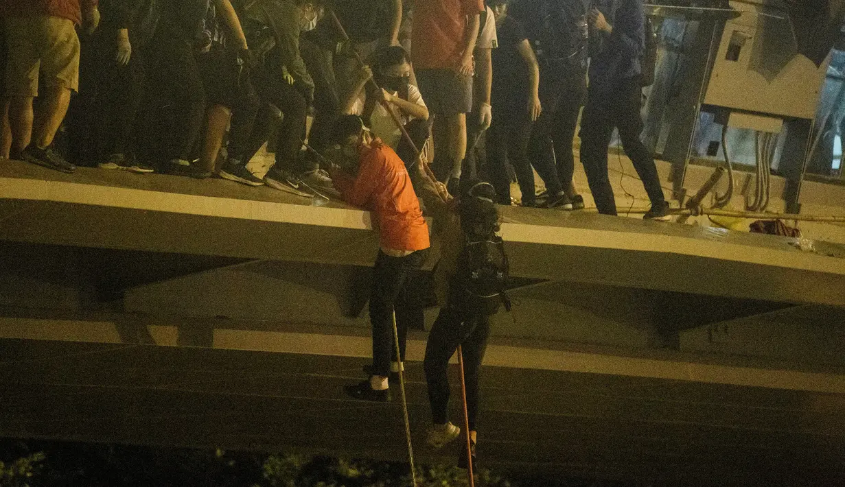 Demonstran menuruni jembatan menggunakan tali untuk melarikan diri dari Universitas Politeknik Hong Kong di Distrik Hung Hom, Hong Kong, Senin (18/11/2019). Lusinan demonstran melarikan diri dari Universitas Politeknik Hong Kong yang dikepung polisi selama berhari-hari. (ANTHONY WALLACE/AFP)