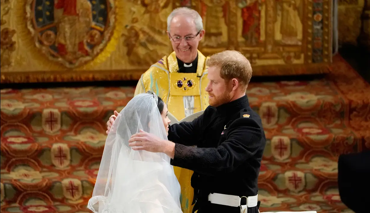 Pangeran Harry membuka tabir Meghan Markle yang disaksikan Uskup Agung Canterbury Justin Welby saat pernikahan mereka di Kapel St. George, Kastil Windsor, Inggris, Sabtu (19/5). Keduanya resmi menjadi suami istri. (Owen Humphreys/pool photo via AP)