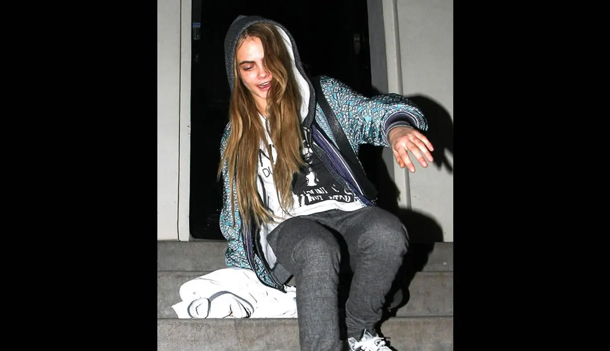Model Cara Delevingne masih tetap tersenyum dan menunjukkan gaya cool ketika terpeleset saat sedang melintasi tangga. (Splash News)