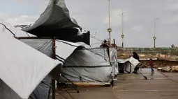 Tinggal di tenda usang dengan kondisi terpal yang compang-camping atau di tengah puing-puing bangunan. Tampak dalam foto, seorang perempuan Palestina pengungsi menyesuaikan terpal tenda keluarga saat wilayah tersebut dilanda hujan dan kondisi musim dingin yang dingin, di Kota Gaza pada 28 Desember 2025. (Omar AL-QATTAA/AFP)