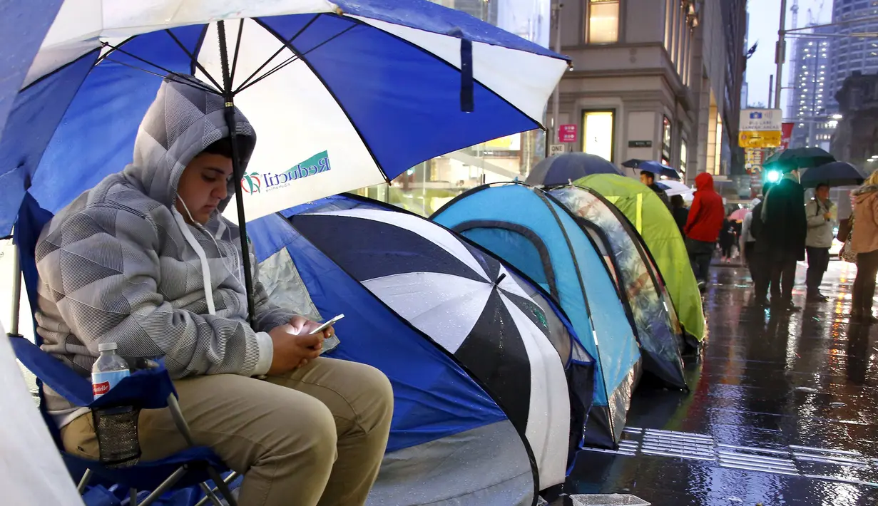 Marcus Barsum melihat iPhone saat ia duduk di bawah payung di luar toko Apple, Sydney, Australia, (24/9/2015). iPhone 6s dibandrol dengan harga sekitar 12 juta - 15 juta rupiah, sedangkan 6s Plus 13 juta - 17 juta rupiah. (REUTERS/David Gray)