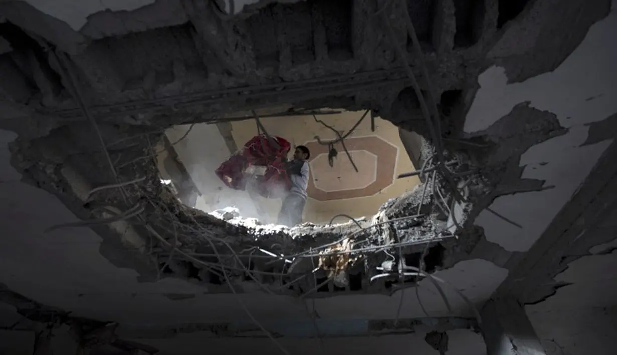 Warga Palestina berusaha memindahkan barang dari salah satu bangunan yang hancur akibat serangan udara militer Israel ke kota Gaza, (12/7/2014). (AFP PHOTO/Mahmud Hams)