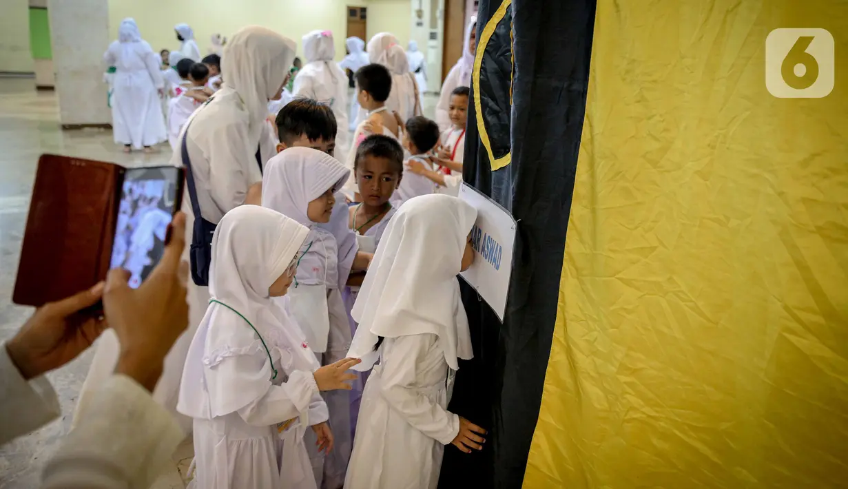 Murid TK melakukan simulasi mencium hajar aswad saat mengikuti edukasi manasik haji anak di Masjid At-Tin, Jakarta, Selasa (28/2/2023). Manasik haji yang diikuti puluhan murid TK se-Kecamatan Pasar Rebo tersebut dalam rangka mengenalkan rukun Islam kelima yakni ibadah haji serta tata cara melaksanakannya kepada anak sejak usia dini. (Liputan6.com/Faizal Fanani)