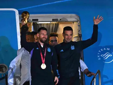 Kapten Argentina Lionel Messi (kiri) memegang Trofi Piala Dunia 2022 bersama pelatih Lionel Scaloni saat turun dari pesawat setibanya di Bandara Internasional di Ezeiza, provinsi Buenos Aires, Argentina (20/12/2022). Argentina tampil sebagai juara Piala Dunia 2022 setelah menumpas Prancis melalui adu penalti di final. (AFP/Luis Robayo)