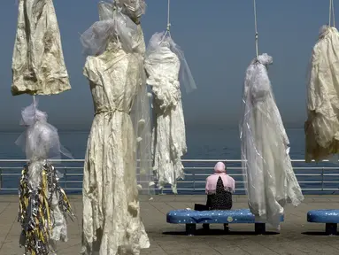 Seorang wanita duduk dekat puluhan gaun pengantin yang digantung di tepi pantai Beirut, Sabtu (22/4). Gaun yang digantung di tepi pantai itu sebagai bentuk protes Undang-Undang Pemerkosaan di Lebanon oleh sekelompok aktivis. (PATRICK BAZ/AFP)