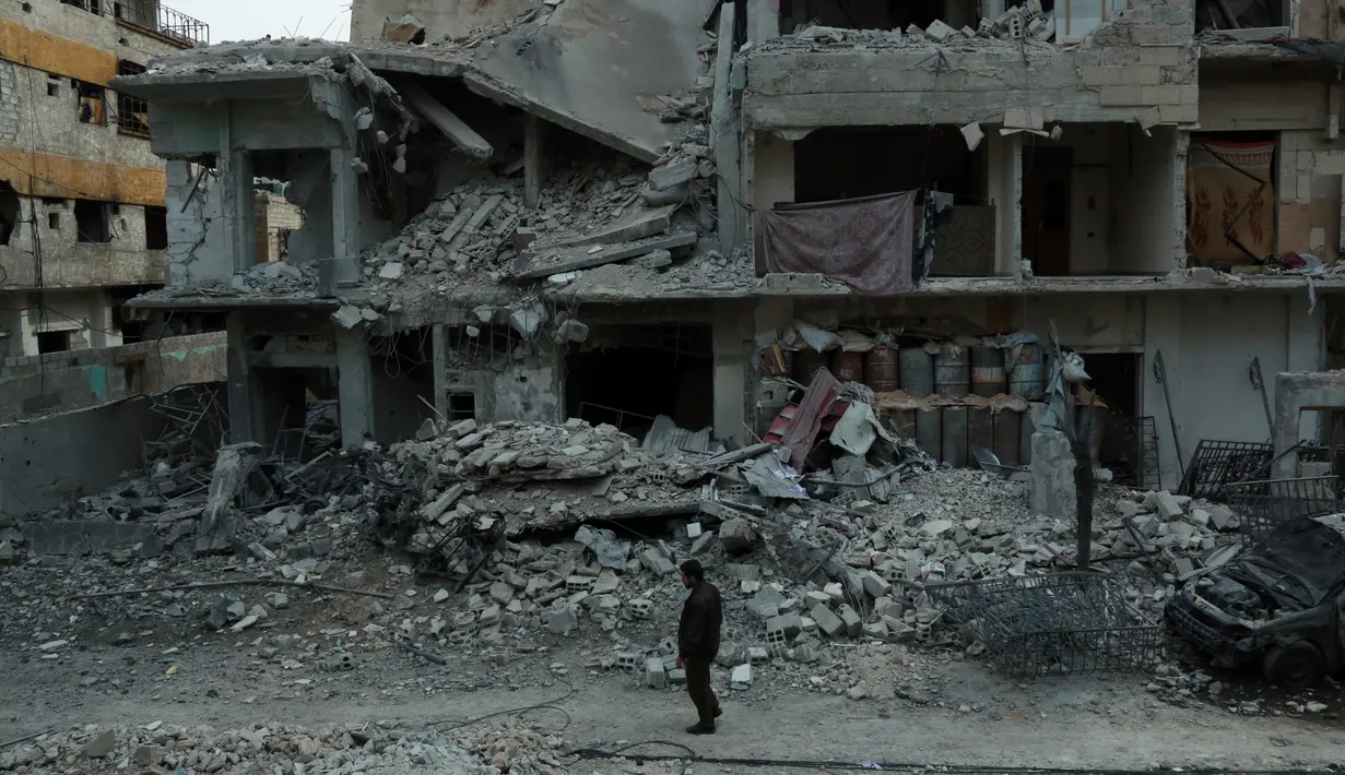 Warga mengamati bangunan yang mengalami kerusakan di Ghouta Timur, Minggu (25/2). Data PBB menyebut ada sekitar 400.000 orang yang masih terjebak dalam perang antara pasukan rezim Suriah dengan pasukan pemberontak di Ghouta Timur. (HAMZA AL-AJWEH/AFP)