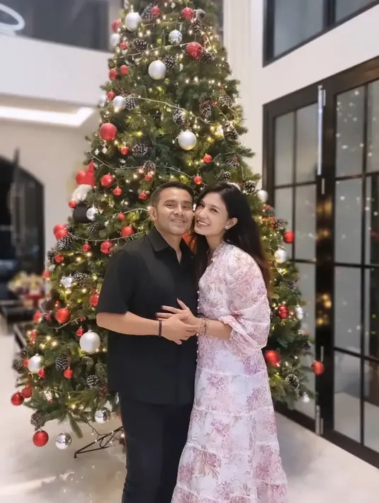 Judika dan Duma Riris merayakan Natal di rumahnya. Judika mengenakan kemeja hitam serasi dengan celananya. Duma mengenakan dress pink bermotif. [@jud1ka]