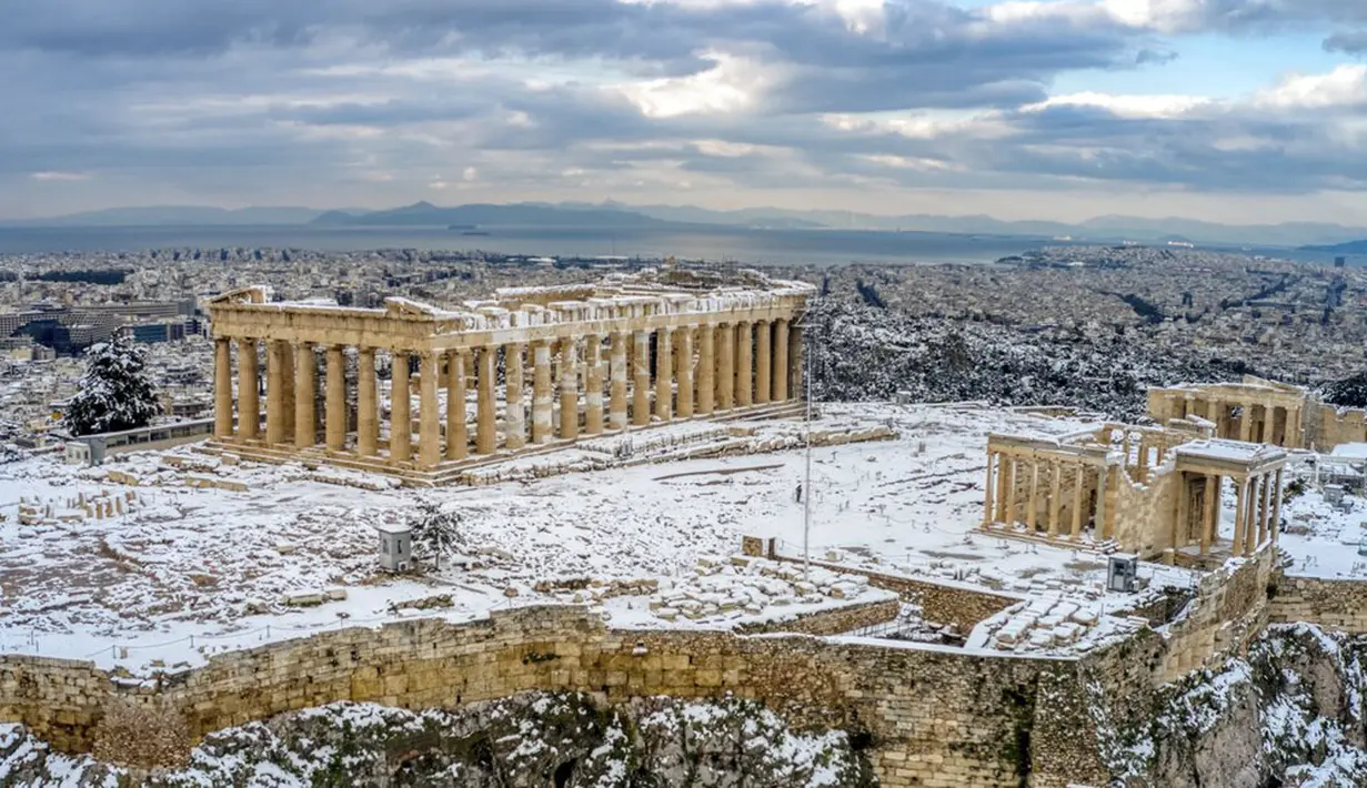 Bukit Acropolis kuno tertutup salju setelah hujan salju lebat di Athena, Yunani, Rabu (17/2/2021). Cuaca ekstrem nampaknya telah membuat suhu di Athena mencapai titik beku dan mengakibatkan salju turun di kota dengan penduduk lebih dari 3 juta jiwa ini. (Antonis Nikolopoulos/Eurokinissi via AP)