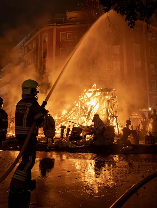 Seorang petugas pemadam kebakaran bekerja saat falla terbakar dalam festival tradisional Fallas di Valencia, Spanyol, Sabtu (19/3/2022). Setiap bulan Maret di Valencia, Spanyol diadakan Festival Fallas. (AP Photo/Alberto Saiz)
