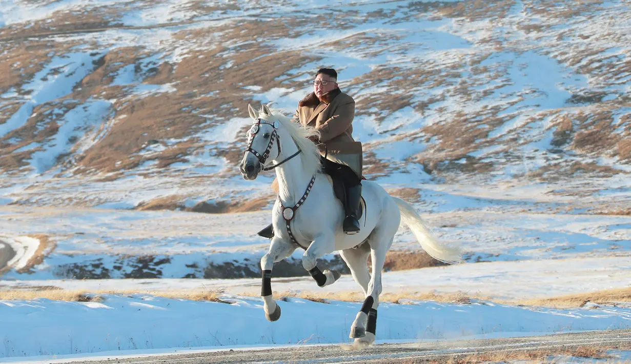Pemimpin Korea Utara Kim Jong-un menunggangi kuda putih  saat salju yang turun di gunung Paektu (16/10/2019). Kim Jong-un tampil mengenakan kaca mata dengan mantel tebal berwarna coklat.  (Photo by STR/KCNA VIA KNS/AFP)