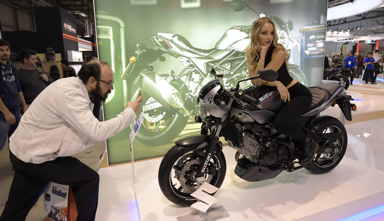 Seorang pengunjung mengambil foto model yang berpose diatas Suzuki SV650X ABS saat pameran Milano Moto Show di Milan, Italia (8/11). Dalam pameran ini berbagai kendaraan roda dua terbaru dihadirkan. (AFP Photo/Miguel Medina)